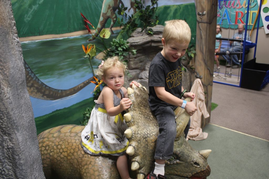 a boy and a girl on a dinosaur at the museum