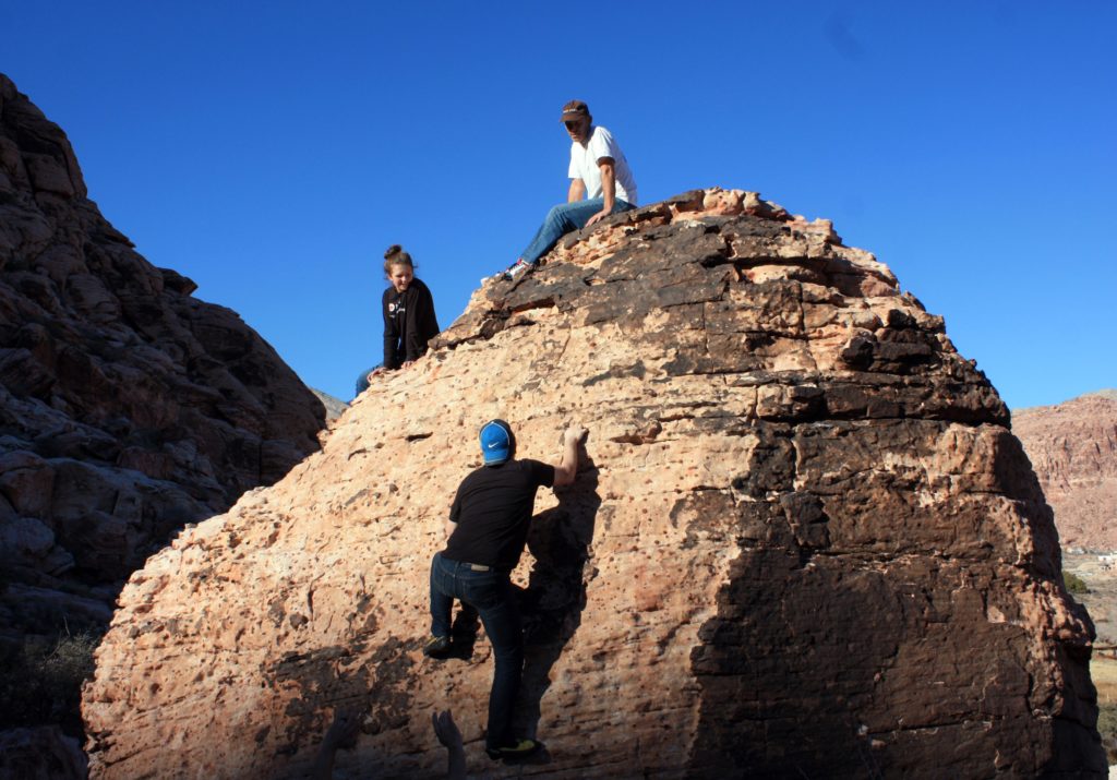 Climber going up a rock face with other climbers at the top of the boulder